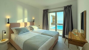 Quarto de hotel com uma cama, mesas de cabeceira, uma escrivaninha e vista para o mar.