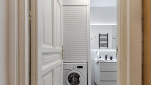 A laundry area with a washing machine, a drying rack, and a sink with a towel. - Waou Salamanca I - Short-Term Rental (Madrid)
