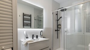 A modern bathroom with a glass-enclosed shower, a white sink with a mirror, and a towel rack. - Waou Salamanca I - Short-Term Rental (Madrid)