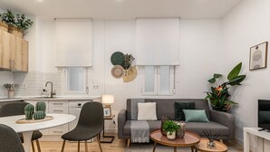 A modern living room with a grey sofa, round coffee table, and a dining area with a white table and chairs. - Waou Salamanca I - Short-Term Rental (Madrid)