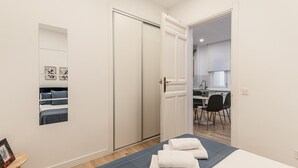 A hotel room with a bed, a small table with a picture frame, a door leading to a bathroom, and a view of a kitchen area. - Waou Salamanca I - Short-Term Rental (Madrid)