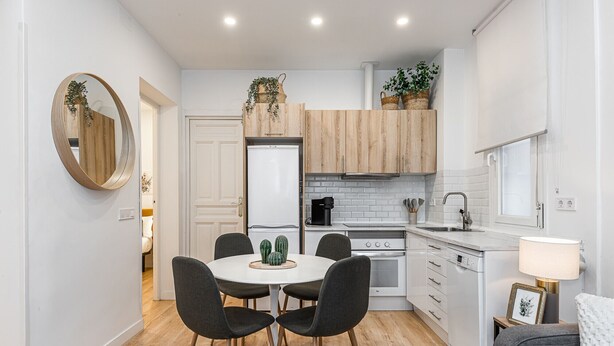 A compact kitchen with a dining area, wooden cabinets, and a white countertop. - Waou Salamanca I - Short-Term Rental (Madrid)