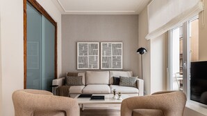 Ein Wohnzimmer mit einer Couch, zwei Sesseln, einem Couchtisch und zwei an der Wand befestigten abstrakten Kunstwerken.