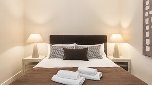 Ein ordentlich bezogenes Bett mit einem braunen Kopfteil, zwei Nachttischlampen, gemusterten Kissen und gefalteten weißen Handtüchern.