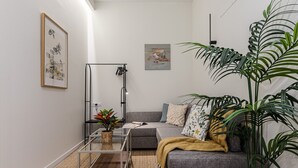 Una sala de estar moderna con un sofá gris, una mesa de centro de vidrio y una planta grande en maceta.
