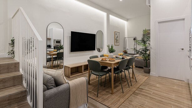 Una sala de estar moderna con comedor, una escalera y una cocina visible a través de un arco.