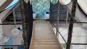 A loft-style bedroom with a sloped ceiling, two beds with striped bedding, a wooden floor, and a view of a green tree through a window. - 🌿 Domaine Saint François – L'Îlot Cocooning (Saint-Hernin)