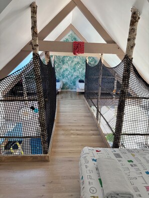 Ein Schlafzimmer im Loft-Stil mit schräg versiegelter Decke, zwei Betten mit gestreifter Bettwäsche, Holzboden und Blick auf einen grünen Baum durch ein Fenster.