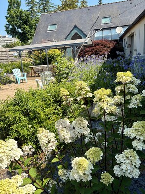 Ein Garten mit Hortensienblüten, einer überdachten Terrasse und Gartenmöbeln.
