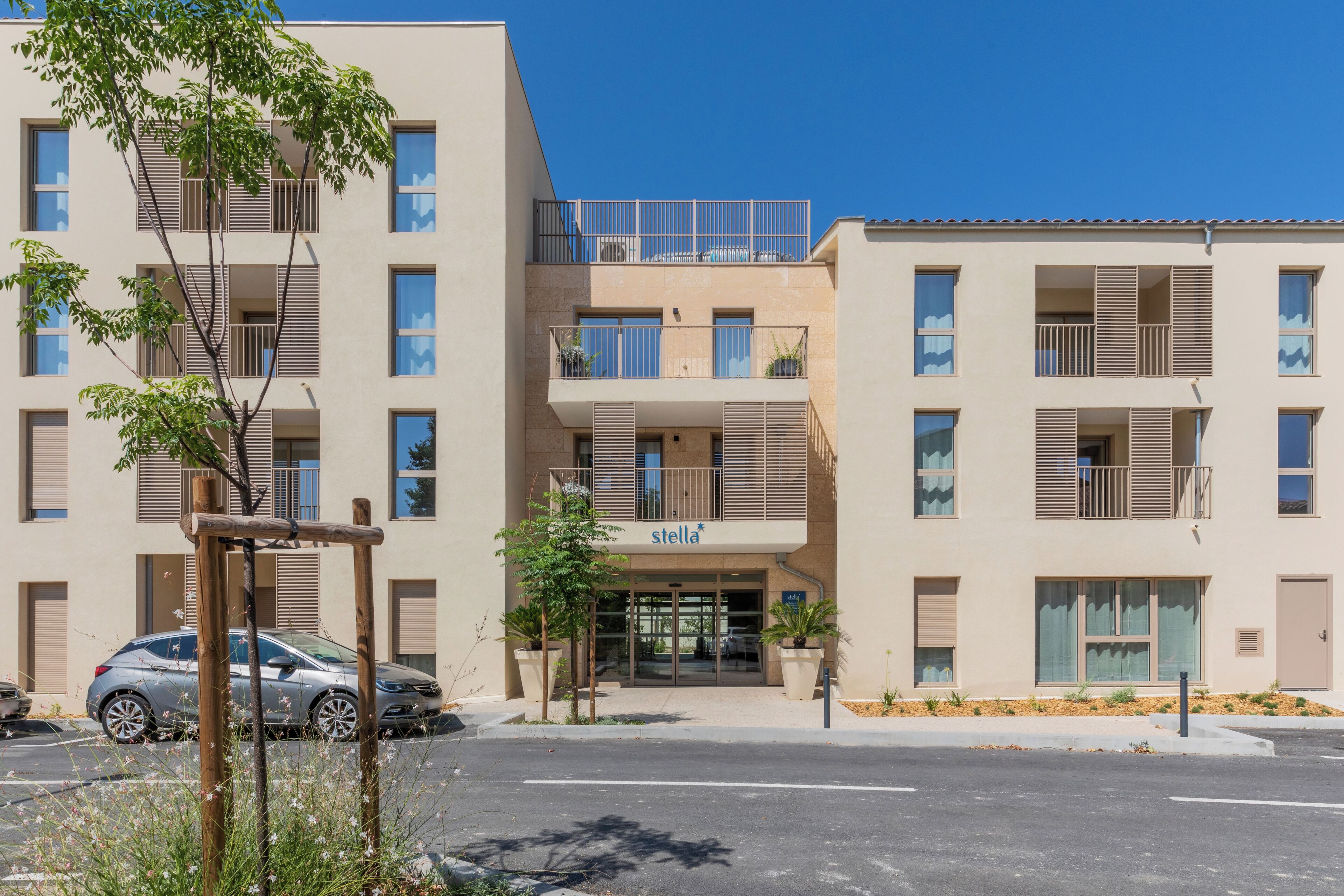 A multi-story residential building with balconies, a ground-level entrance, and a parking area.