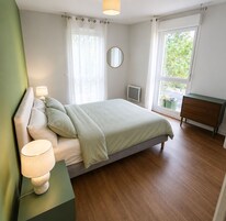 Un dormitorio con cama, lámparas de noche, cómoda, espejo y ventana con vista a follaje.