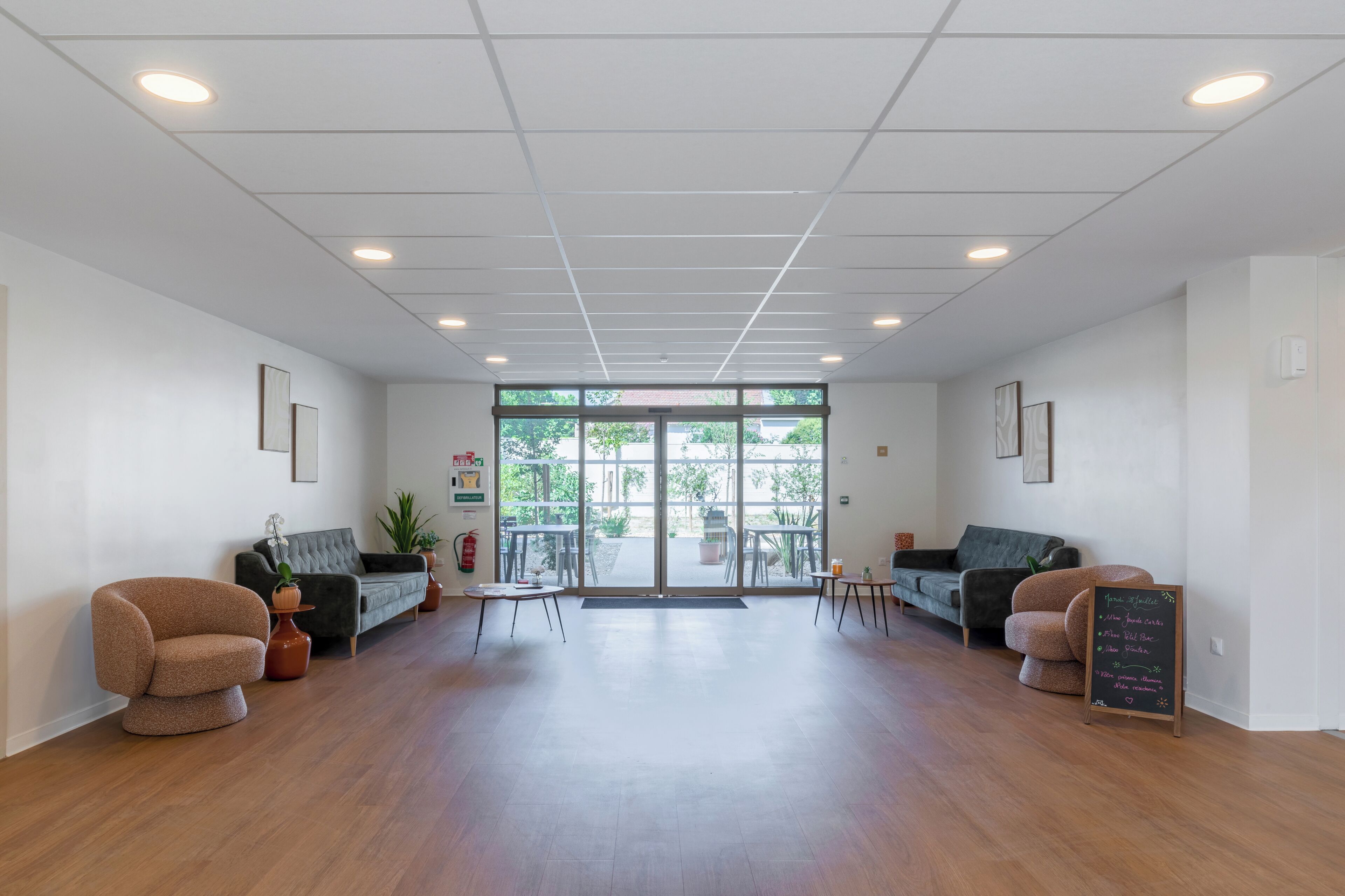 A spacious lobby with a wooden floor, two sofas, a small table, and a glass door leading outside.