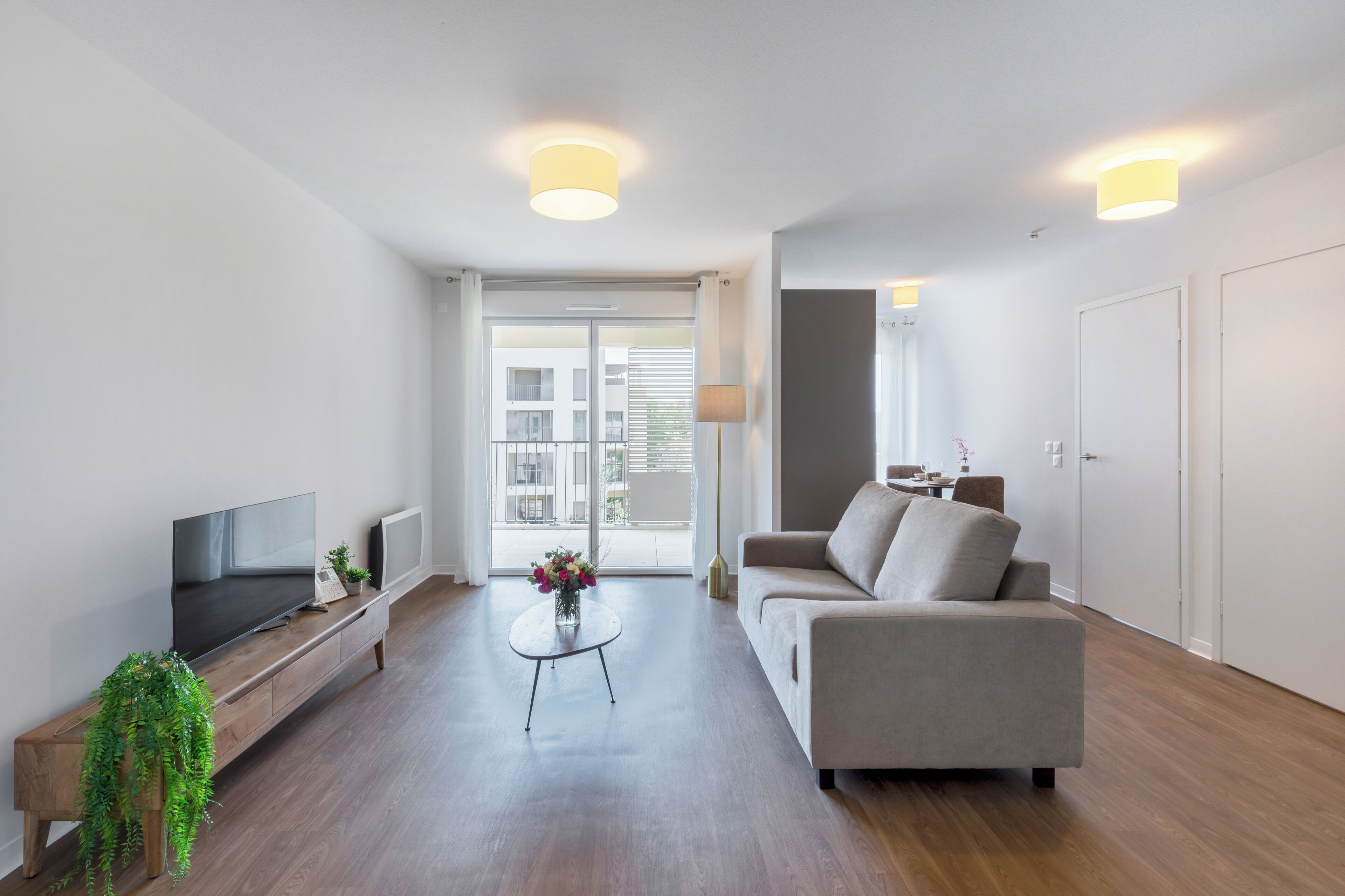A modern living room with a flat-screen TV, a sofa, a coffee table, and a potted plant.