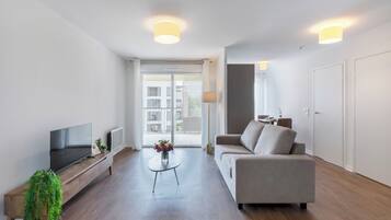 A modern living room with a flat-screen TV, a sofa, a coffee table, and a potted plant.