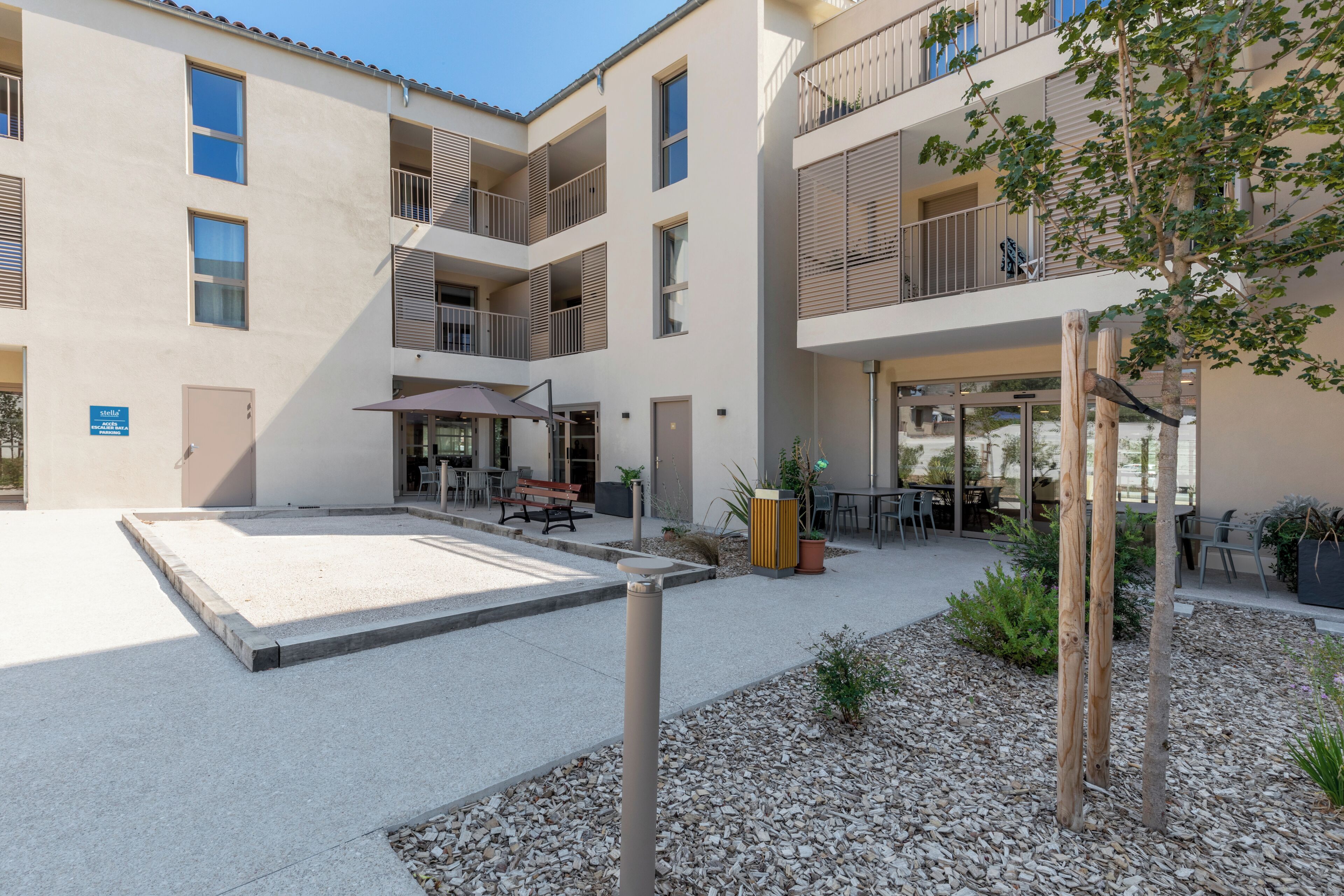 Un edificio de varios pisos con un patio que cuenta con asientos al aire libre, un basurero y una maceta de madera.