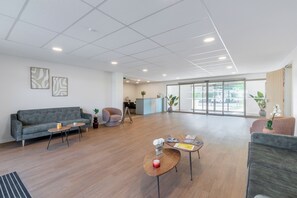 A spacious, modern interior with a grey sofa, a coffee table, and a seating area with a plant. - Zenao Appart'hôtels Beaucaire (Beaucaire)