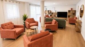 A modern living room with orange sofas, a green sofa, a wooden coffee table, and a TV.