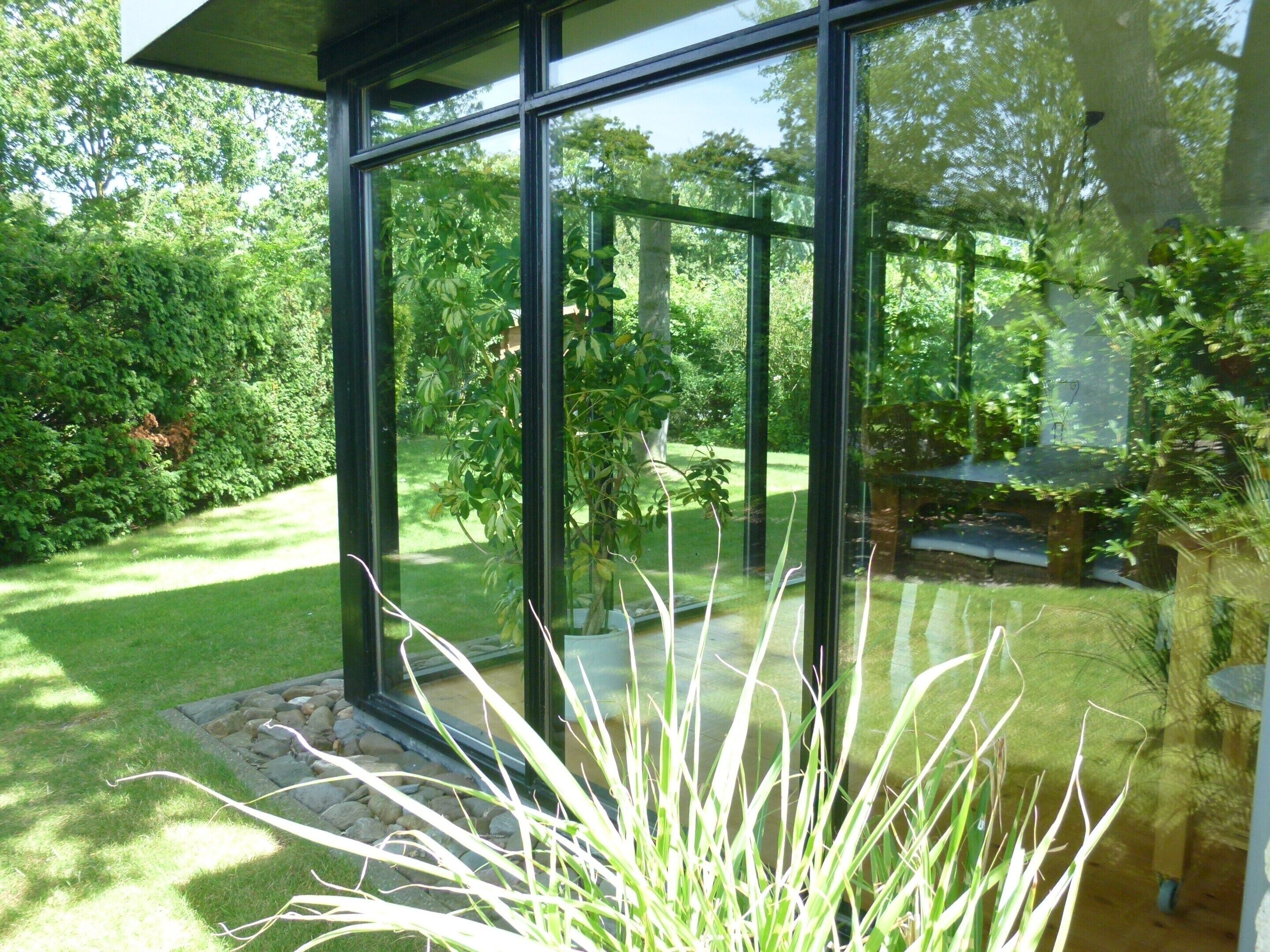 Een modern gebouw met grote glasramen, een verzorgde tuin en een vijver.