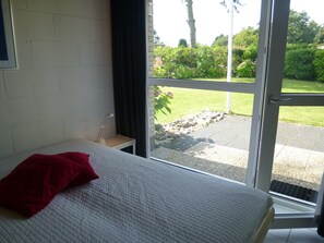 A bedroom with a bed, a nightstand, and a window with a view of a garden. - Detached Bungalow, Perfect for Water Sports and Nature Enthusiasts (Kamperland)