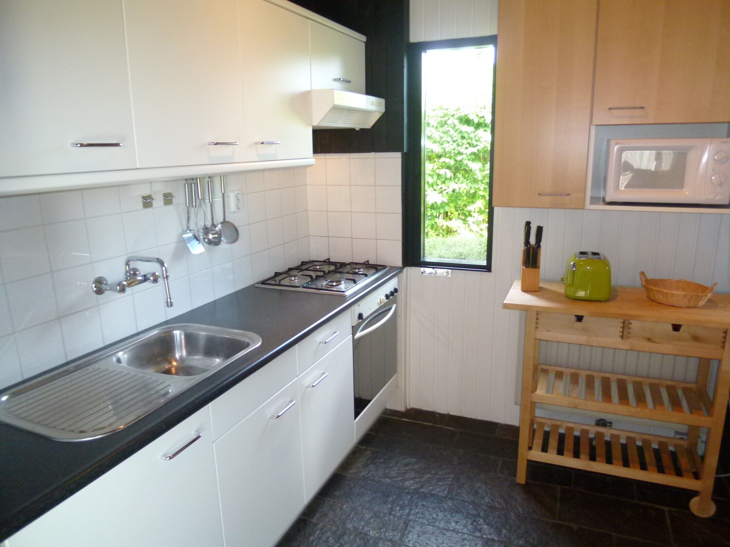 Een keuken met witte kastjes, een RVS-spoelbak, een gasfornuis en een magnetron.