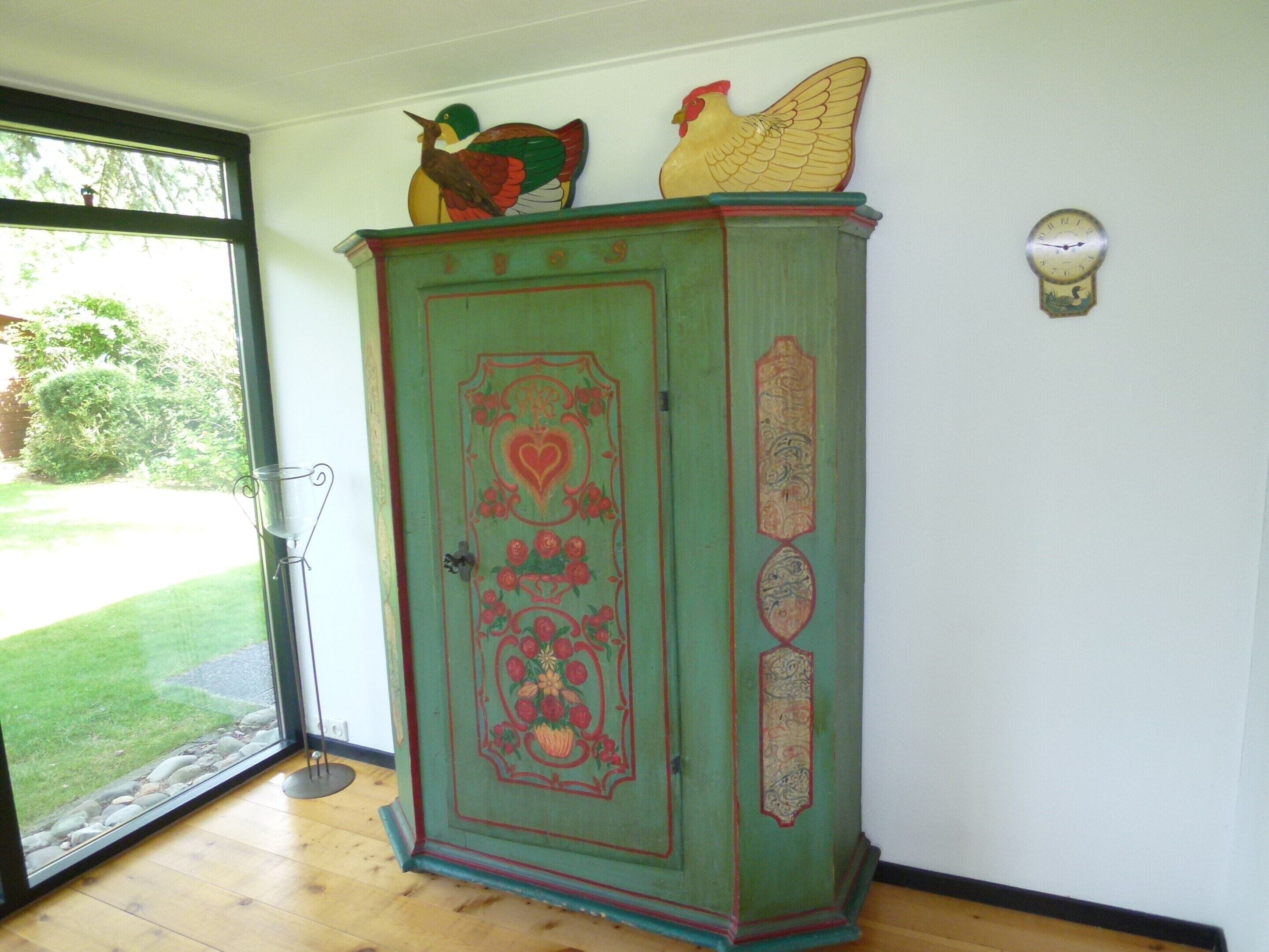 Een groene kast met decoratieve details en een klok aan de muur.