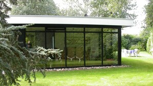A modern building with large glass windows, a grassy lawn, and a dining area with outdoor furniture. - Detached Bungalow, Perfect for Water Sports and Nature Enthusiasts (Kamperland)