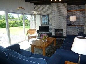 A living room with a fireplace, a television, and a large window. - Detached Bungalow, Perfect for Water Sports and Nature Enthusiasts (Kamperland)