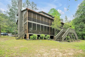 A two-story building with a balcony, a staircase leading to the upper level, and a grassy yard.