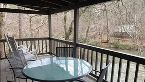 Un espace extérieur abrité, avec une table en verre et des chaises en métal, offrant une vue sur une rivière et une zone boisée.