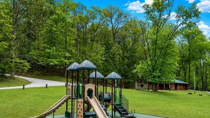 Une aire de jeux avec des toboggans et des structures d’escalade, entourée d’une pelouse et d’arbres.