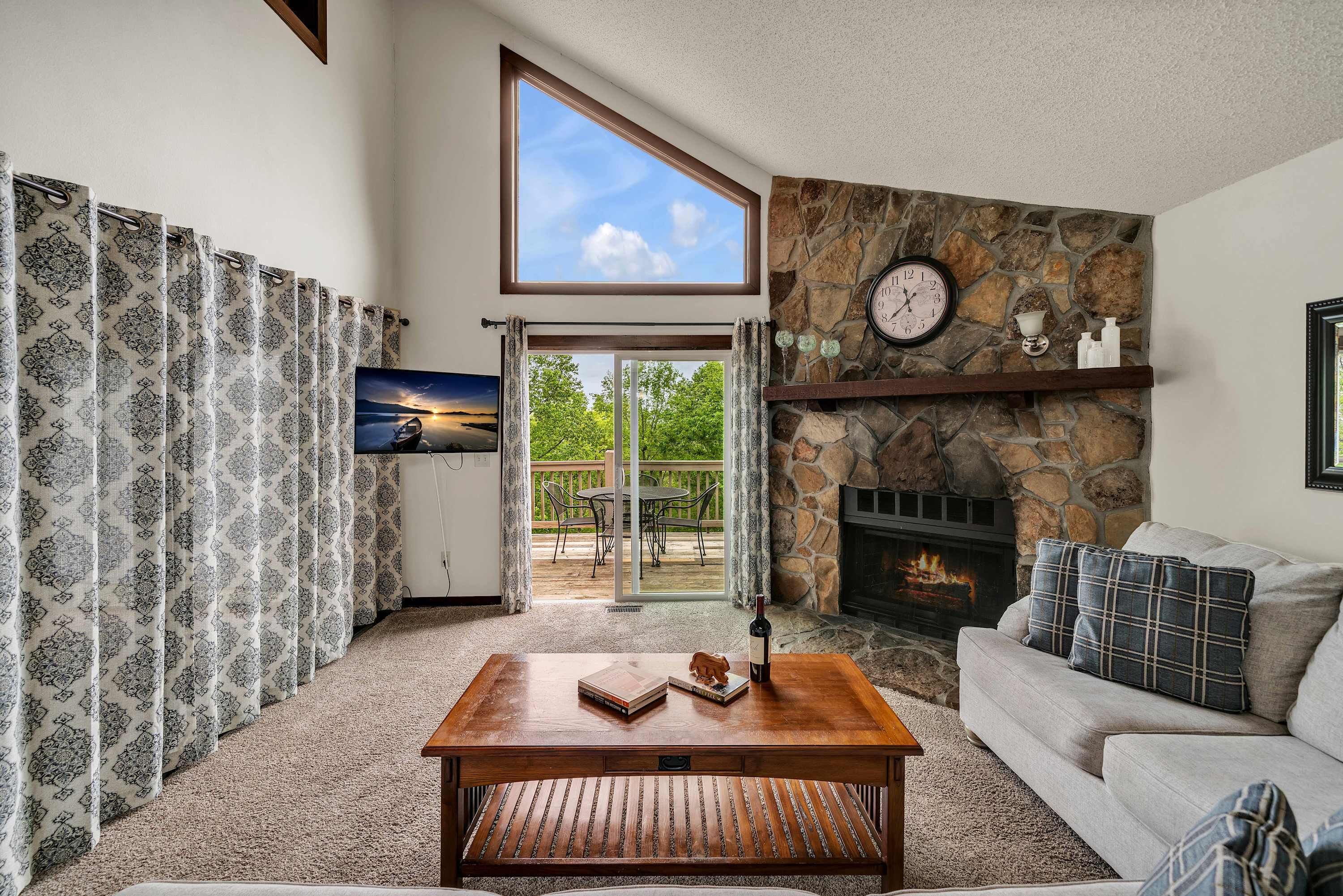 A living room with a stone fireplace, a sofa, a coffee table, and a view through a glass door to an outdoor patio.