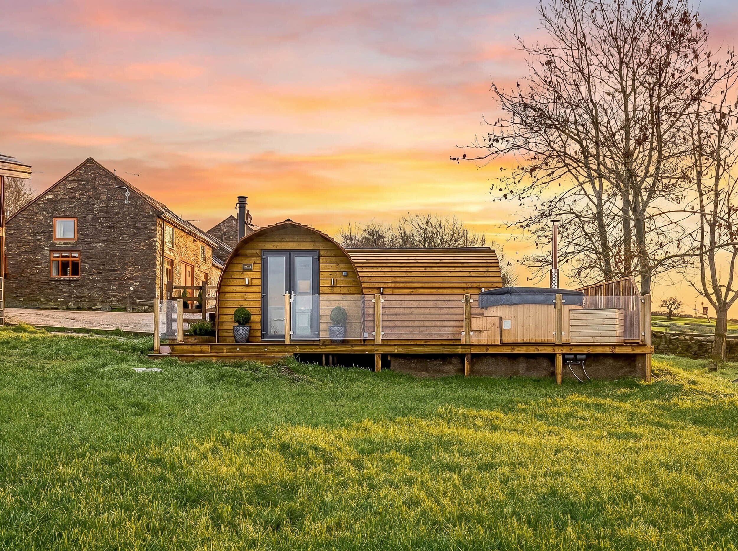 Ein rustikales Blockhaus mit einer Holzterrasse, ein Steinhaus und ein Baum im Hintergrund.