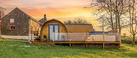 Une cabane rustique avec une terrasse en bois, un bâtiment en pierre et un arbre en arrière-plan.