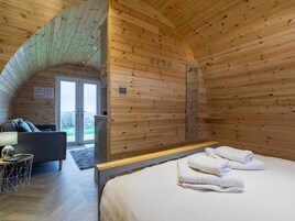 Una camera in una baita di legno con un letto, un divano, un tavolino e una porta che dà sull'esterno.