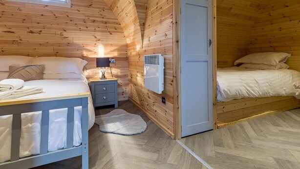 Una camera da letto accogliente in una baita di legno, con due letti, un comodino, una lampada e una finestra.