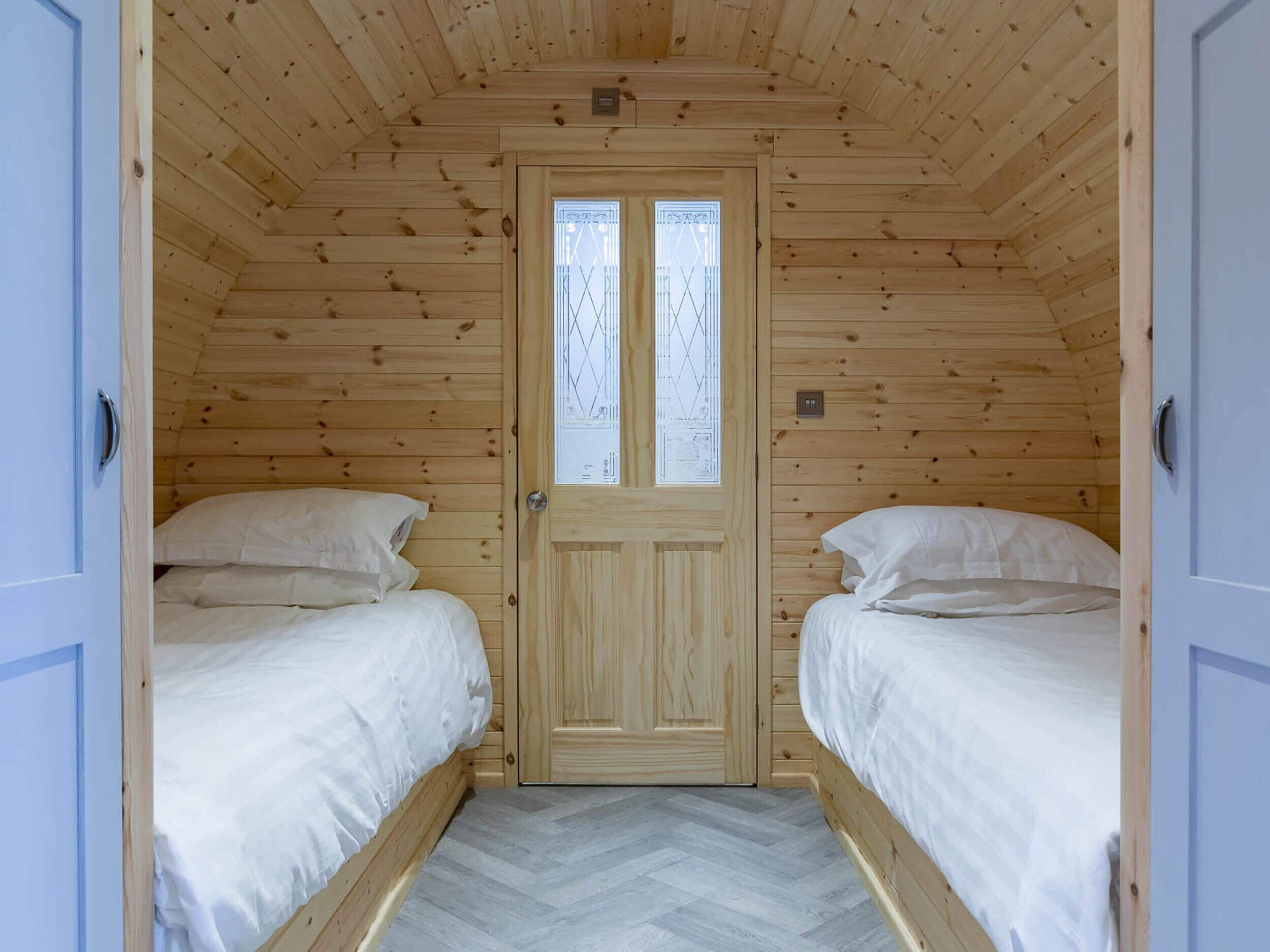 A room with two beds, a wooden door, and a herringbone-patterned floor.