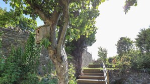 Eine Steintreppe führt zu einer hölzernen Struktur, umgeben von Grünpflanzen und einer Steinmauer.