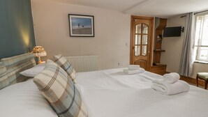 Ein Hotelzimmer mit einem Bett, einem gerahmten Bild an der Wand, einer Heizung, einer Holztür und einem an der Wand befestigten Fernseher.