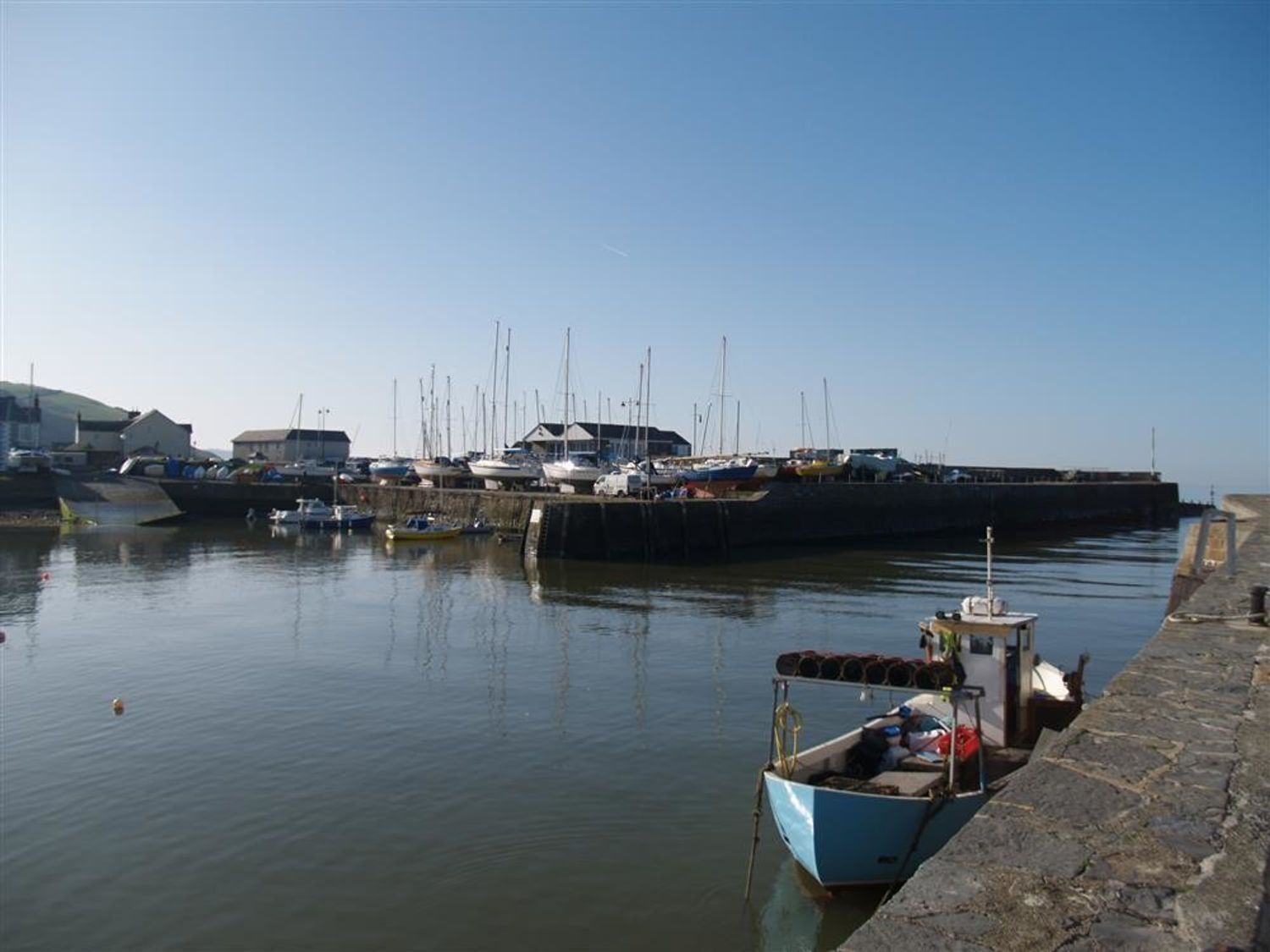 A harbor with boats docked, a stone quay, and buildings in the background.