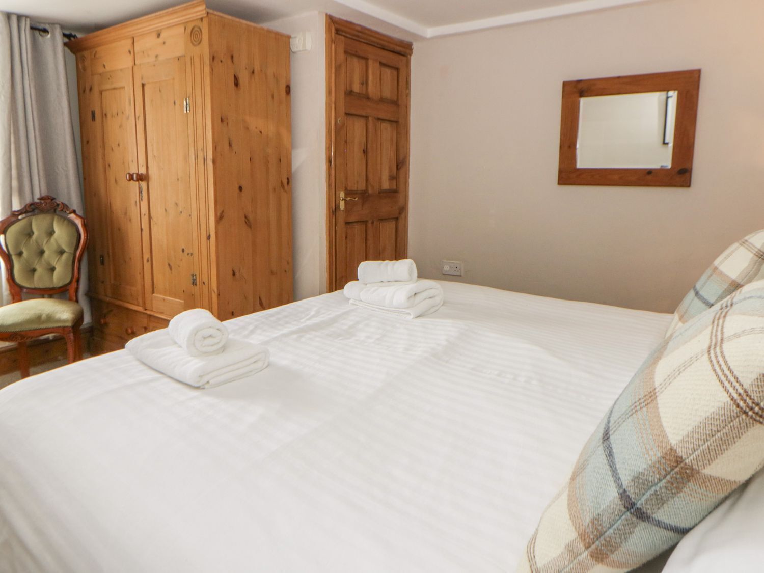 A bedroom with a large bed, a wooden wardrobe, a chair, and a mirror on the wall.