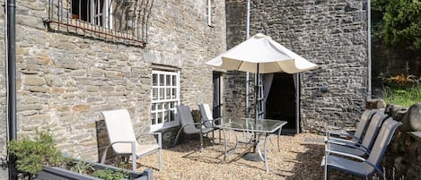 A stone building with a balcony, outdoor seating, and a table with an umbrella.