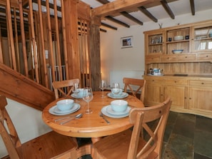 A wooden dining table with chairs, a kitchen with wooden cabinets, and a staircase with wooden railings. - Dewi Villa Apartment (Aberaeron)