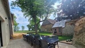 Eine Terrasse im Freien mit einem langen Tisch, Stühlen, einer Steinmauer und einem Rasen.