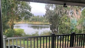 Une vue depuis une terrasse couverte, dotée d’une balustrade, donnant sur un lac paisible entouré d’arbres.