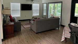 Un salon avec un canapé, une table recouverte d’une nappe à rayures, une lampe et un ventilateur de plafond.