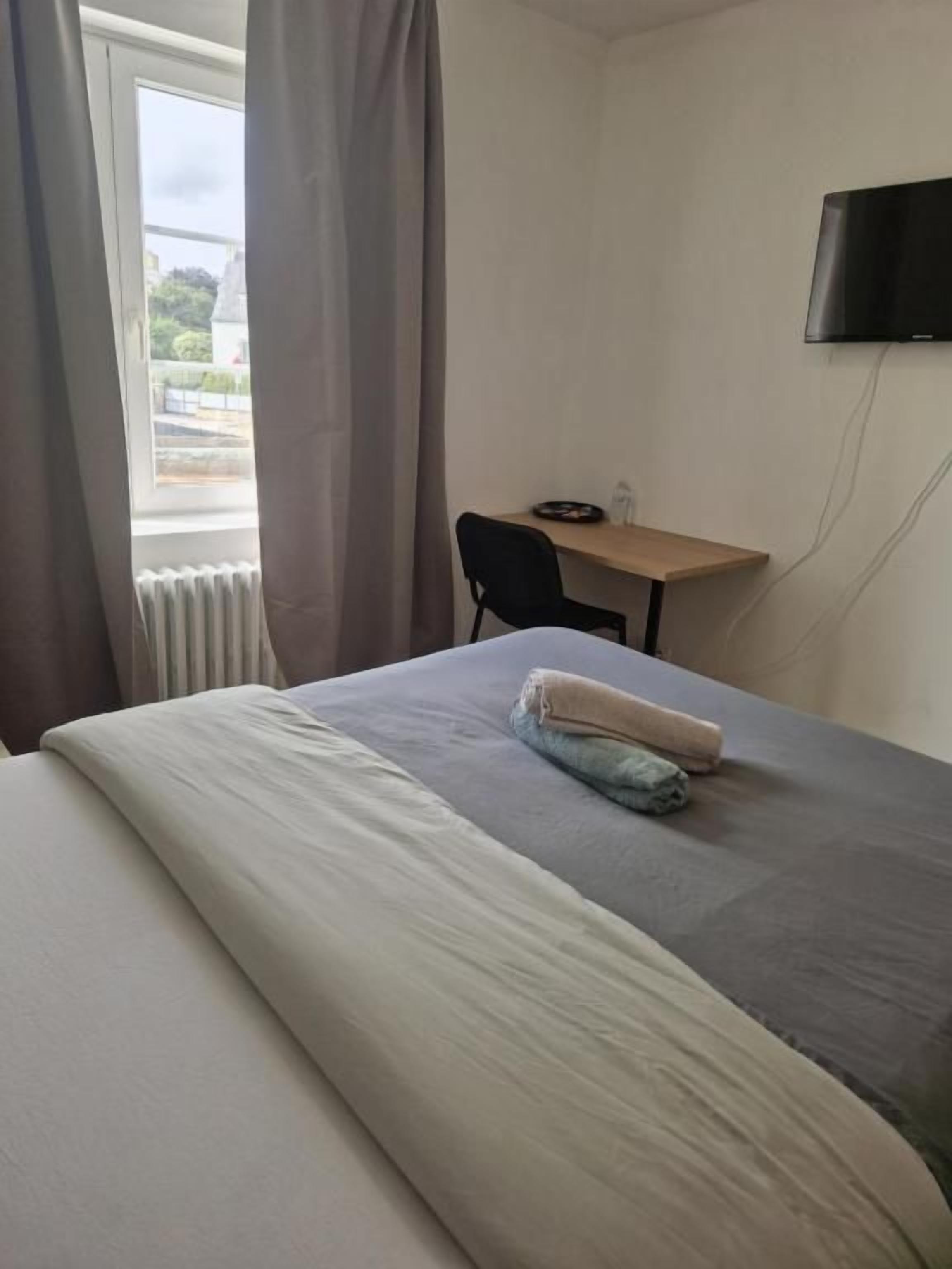 A hotel room with a bed, a desk, a chair, and a television.