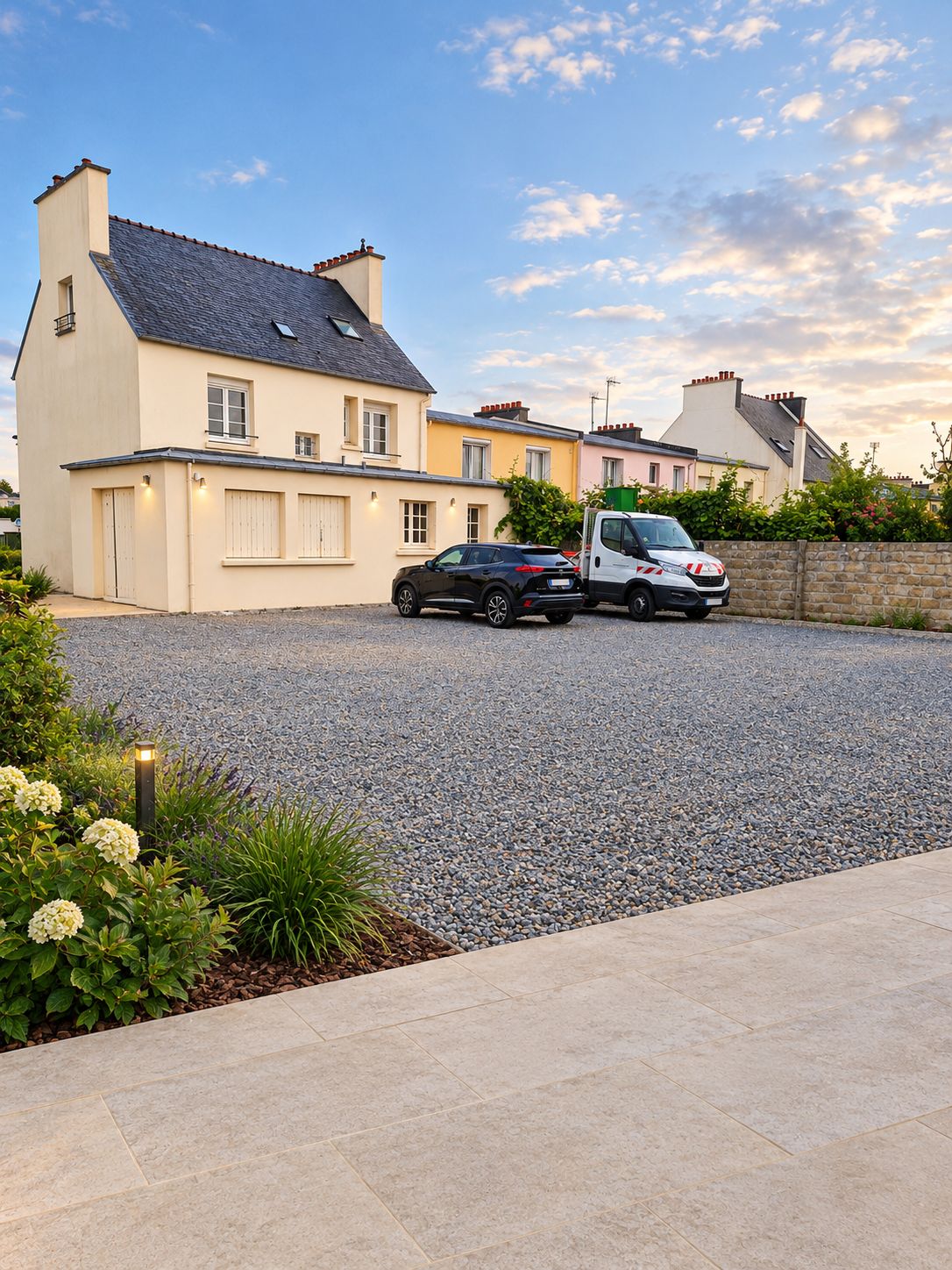 A residential area with houses, a gravel driveway, and parked cars.