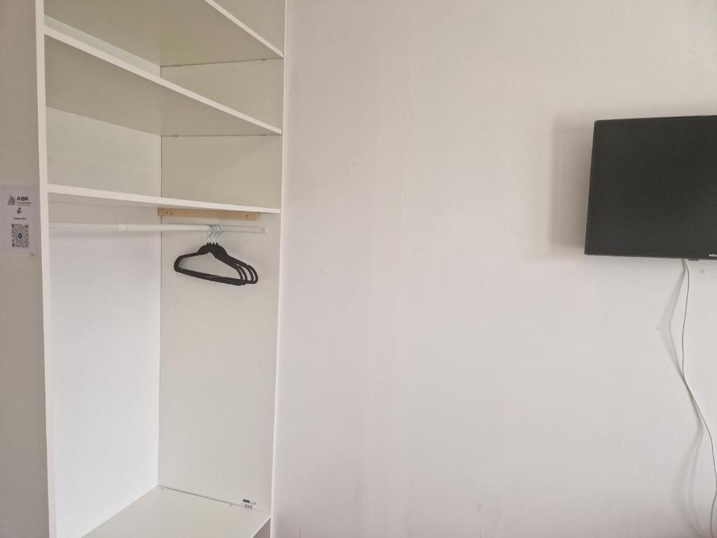 A white closet with shelves and a hanging rod, a black television mounted on the wall, and a power cord.