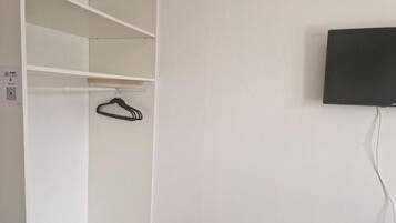 A white closet with shelves and a hanging rod, a black television mounted on the wall, and a power cord.