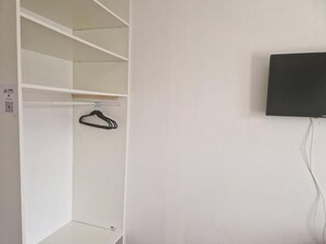 A white closet with shelves and a hanging rod, a black television mounted on the wall, and a power cord.